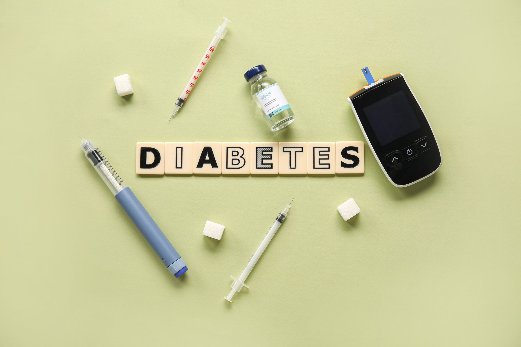 Word DIABETES with Glucometer, Insulin, Lancet Pen and Sugar on Green Background. Diabetes Concept